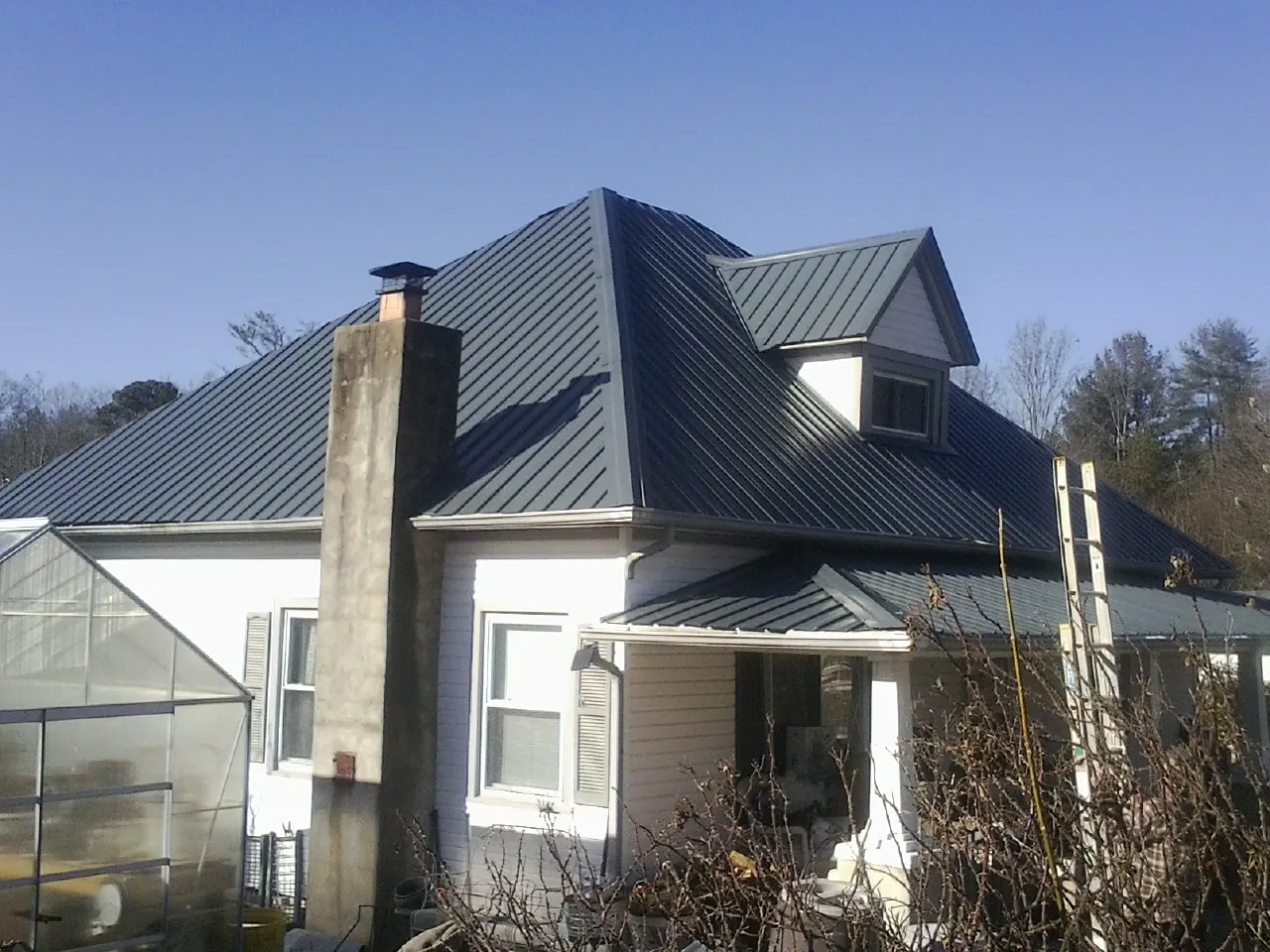 Dark blue standing seam metal roof on a white farmhouse with dormer — Slate & Tile Roof Repair by Roofing Brothers in Cleveland